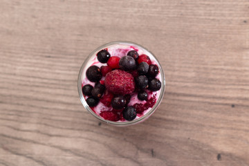 Raspberries, blueberries, blackberries mixed with natural yogurt inside a small glass on a wooden table