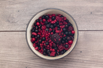 Raspberries, blueberries, blackberries in a round bowl on a wooden table