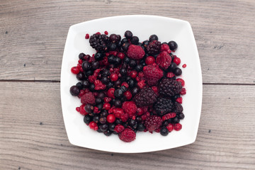 Raspberries, blueberries, blackberries in a white plate on a wooden table