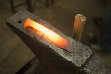 Red hot hand forged steel knife on anvil in blacksmith shop