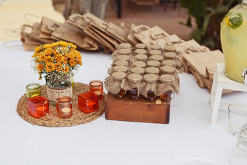 Decorate composition on a festive table. Candy bar in rustic style. Beautiful orange flowers, candles and little jars of honey
