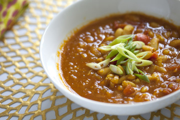 Bean and tomato soup with green onions on gold placemat