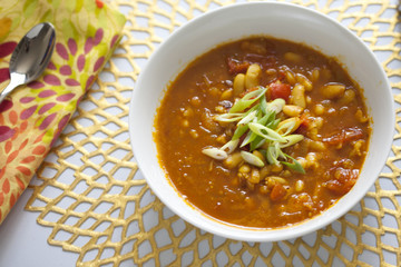 Bean and tomato soup with green onions on gold placemat