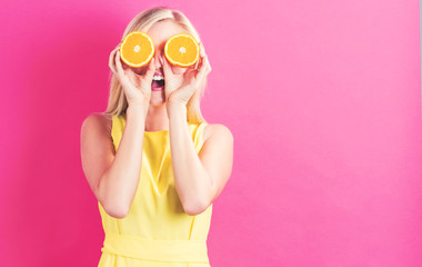 Happy young woman holding oranges halves on a pink background