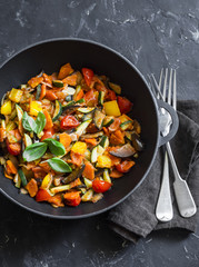 Quick ratatouille in a cast iron skillet on a dark background, top view. Steamed vegetables -...