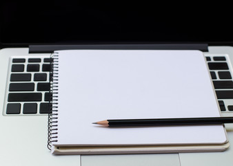 Black pencil on notepad and laptop computer