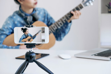social media learning concept, relaxing and playing guitar, Young woman concentrating learn and play the guitar to a tutorial on lesson online, while she recording music video in camera at home - obrazy, fototapety, plakaty