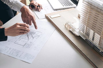 Engineering or Creative architect in construction project, Engineers hands working with compasses on construction blueprint building model at a workplace in office, Building and architecture concept