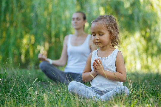 Young mother and cute little daughter meditating in lotus pose together