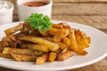 Homemade french fries serve with ketchup and sour cream or mayonnaise. Golden brown crispy french fries sprinkle with salt and oregano on white plate for snack or appetizer.French fries on wood table.