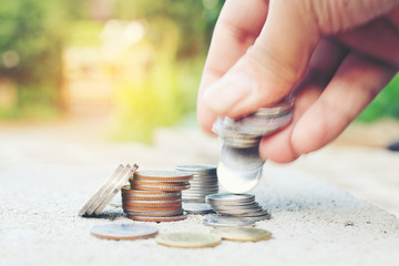 Man's hand put money coins to stack of coins over blurred image of green nature abstract background with vintage tone filter. Money, Financial, Business Growth concept.