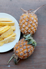 Cutting fresh pineapple and pineapple shelled Asian-style in white dish on the old wooden background. Tropical fruit concept.