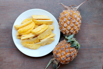 Naklejka na ściany i meble Cutting fresh pineapple and pineapple shelled Asian-style in white dish on the old wooden background. Tropical fruit concept.