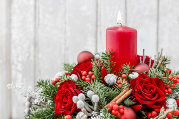 Christmas decoration with candle, red roses, fir, brunia and cinnamon sticks.
