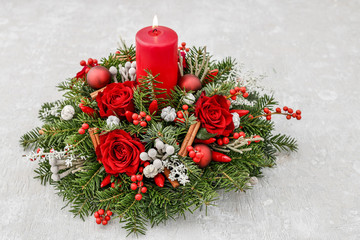 Christmas decoration with candle, red roses, fir, brunia and cinnamon sticks.