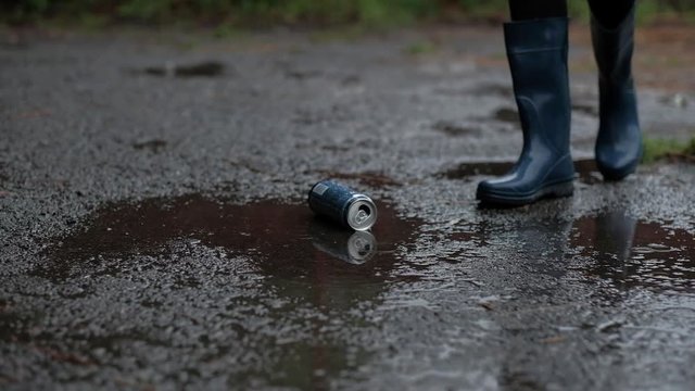 Closeup - Girl in Blue Rubber Boots and Black Legency Crushes a Tin Can From Beer, in Rainy Weather, Stop Alcoholism, Bad Habit