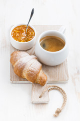 Coffee with fresh croissant and jam on a wooden board, vertical