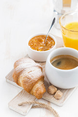 Coffee with fresh croissant, orange juice and jam on a wooden board, vertical