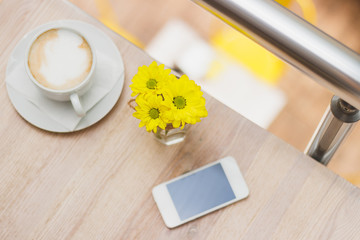 Cup of cappuccino, phone and bouquet of yellow flowers