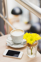 Cup of cappuccino, phone and bouquet of yellow flowers