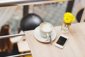 Cup of cappuccino, phone and bouquet of yellow flowers