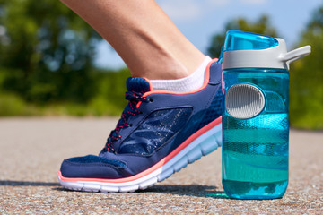 Sports bottle and legs in sneakers stand on road