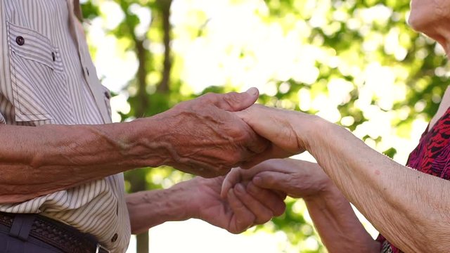 Close-up of grandma and grandpa holding hands, outdoors, wrinkled hands of an elderly couple close-up.