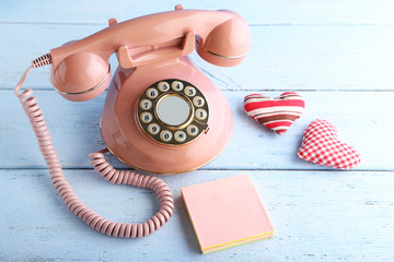 Pink retro telephone with sticky notes and hearts on white wooden table