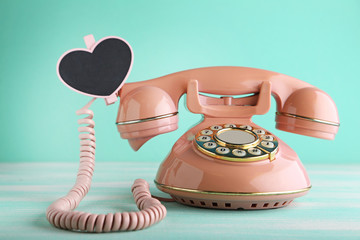 Pink retro telephone with heart on green wooden table