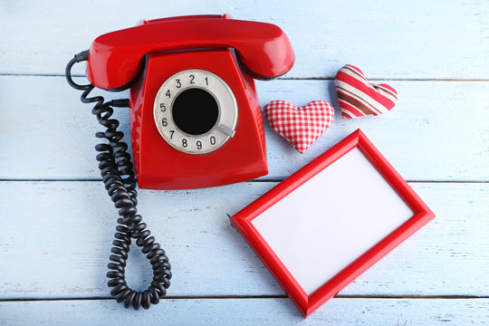 Red retro telephone with photo frame and hearts on white wooden table
