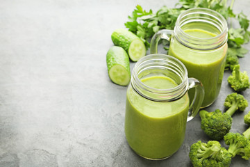 Bottles of juice with broccoli and cucumber on grey wooden table