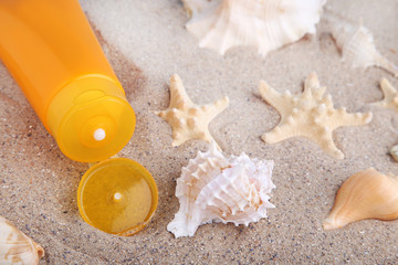 Obraz na płótnie Canvas Sunscreen with seashells on beach sand
