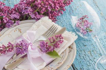 Obraz na płótnie Canvas Tableware and silverware with bunches of violet lilac on the wooden background