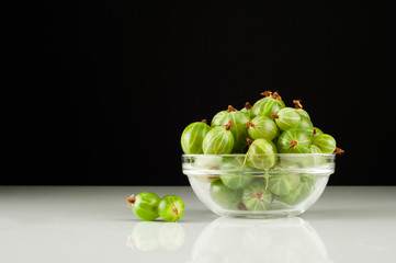 Juicy ripe berries of a gooseberry in a small glass plate on black surface. Gooseberry harvest