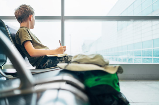 Boy waits departure time in airport and writes in notebook