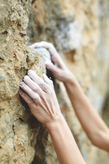 woman climber is preparing to climb on the rock. hands in chalk on the rock close up