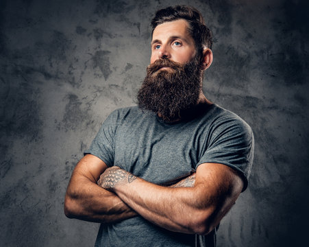 Bearded male with tattoos on arms over grey background.