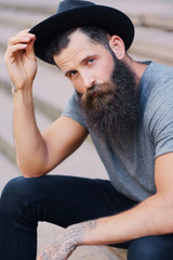 A man in a hat with tattoos on arms, sits on a step.