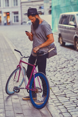 A man holds single speed bicycle and using a smartphone.