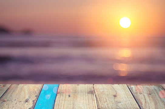 Blur beautiful tropical sunset beach with bokeh sun light wave on copy space empty old wood table abstract background.