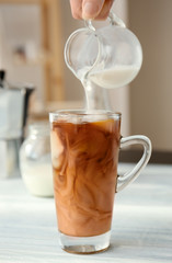 Pouring milk into glass cup with cold brew coffee on light background
