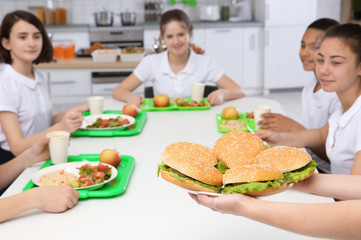 Woman serving plate with delicious sandwiches to children at school canteen