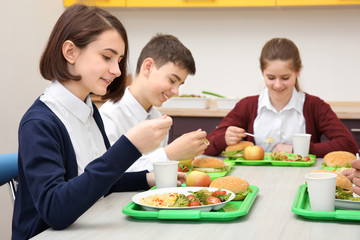 Children sitting at table in school cafeteria while eating lunch