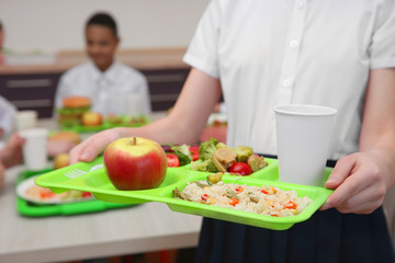 Girl holding tray with delicious food in school canteen, closeup