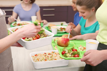 Young woman serving lunch to children at school canteen