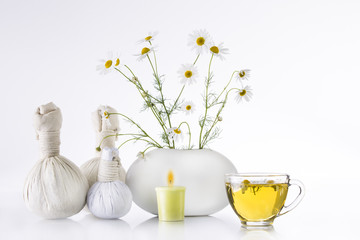 Bouquet of chamomiles flowers in a white vase and a transparent cup with tea on a white background. Herbal balls, spa.