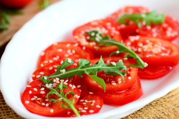 Fresh tomato slices, arugula rocket and sesame seeds salad. Low calorie salad on a white plate and burlap napkin. Diet lunch or dinner idea. Closeup