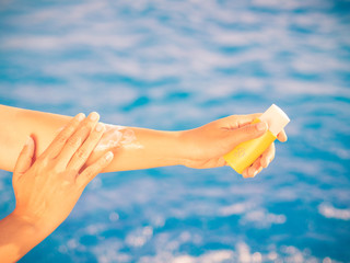 Woman hand apply sunscreen / sunblock by the swimming pool. Vacation and relaxation, summer travel concept.