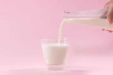 Keuken foto achterwand Milkshake Pouring milk in to glass from bottle on a pink