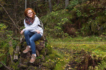 Girl traveler in jeans with a backpack sits on logs in the forest